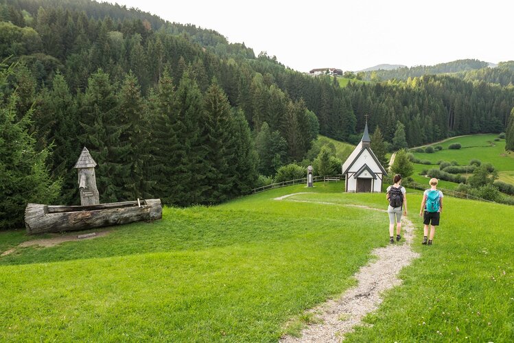 Zwei Frauen gehen einen Wanderweg und gehen auf eine Kapelle zu.